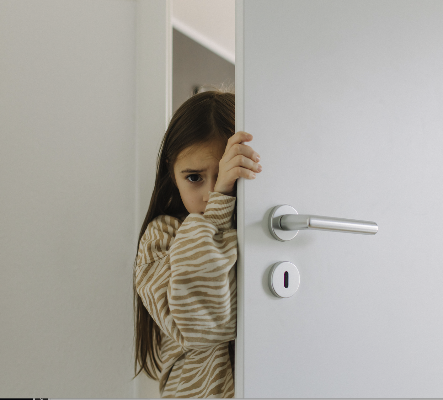 A child looking out from behind a partially opened door
